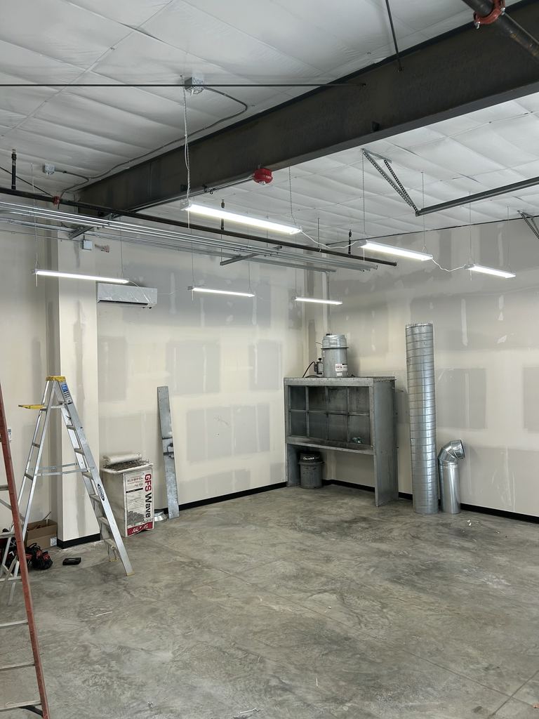 Open commercial unit with a concrete floor, suspended LED light fixtures and ladders, ready for the next stage of work