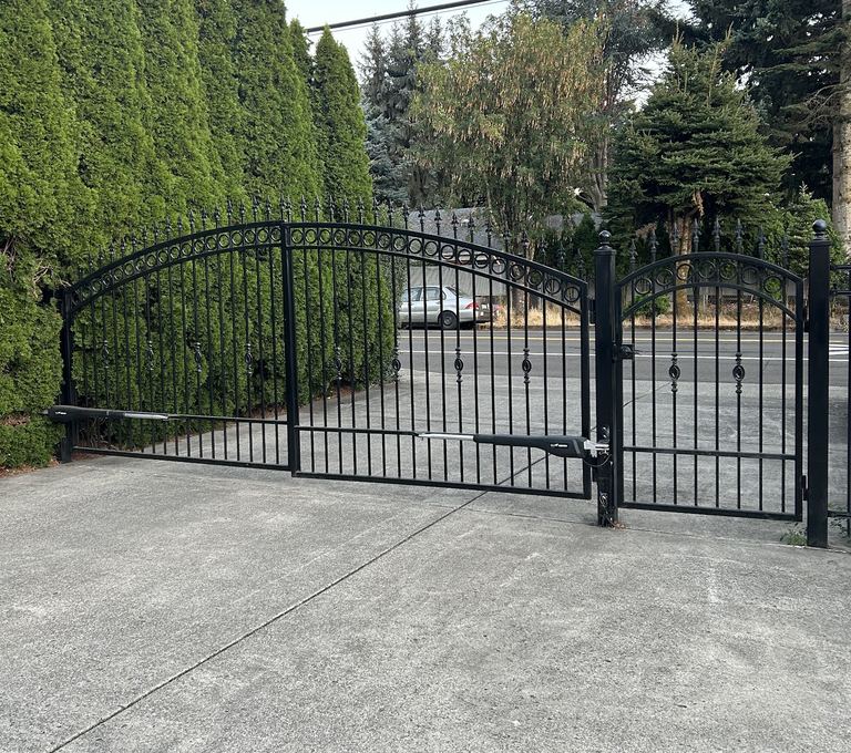 Black wrought-iron double driveway gate fitted with automatic gate operator arms