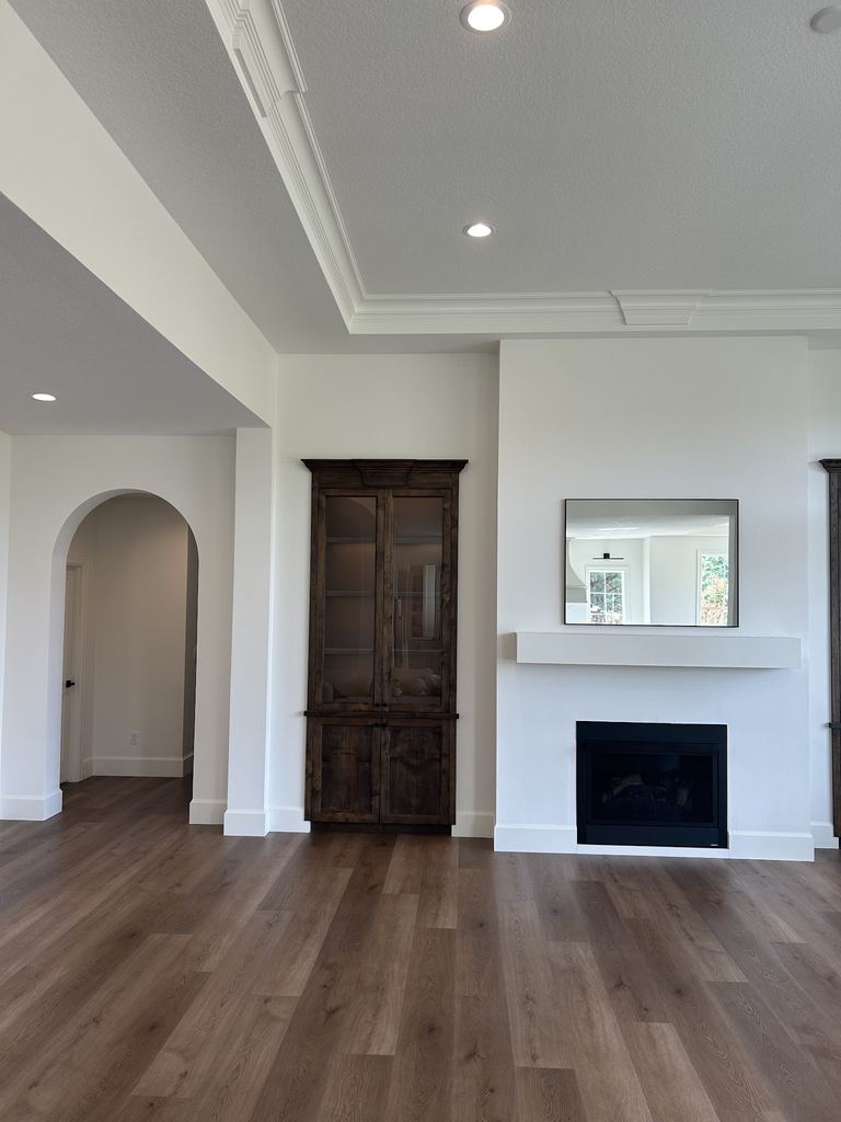 Empty living room with wood floors, a fireplace and recessed ceiling lights in a tray ceiling