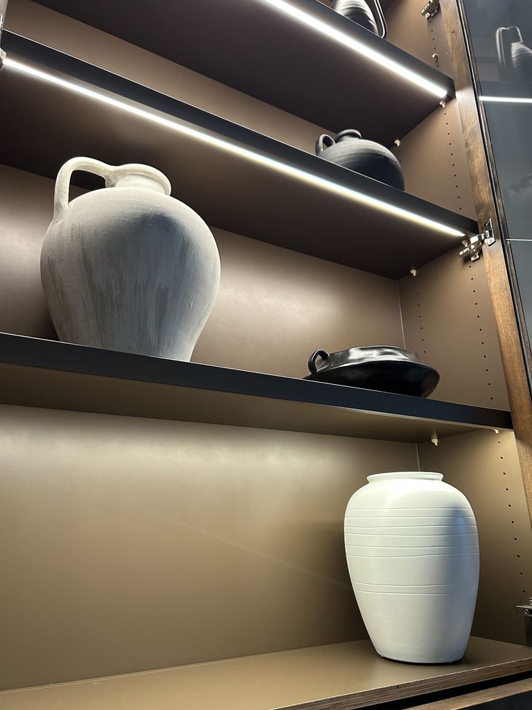 Close view of dark wood shelving with LED strip lights washing light down over ceramic vases
